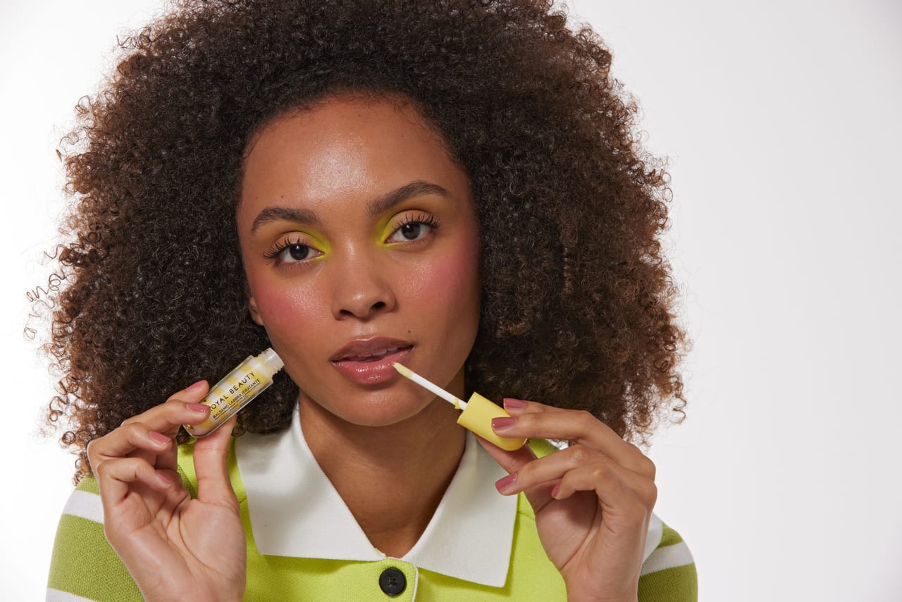 Modella con capelli afro e trucco occhi giallo e rosa, prodotto in mano.