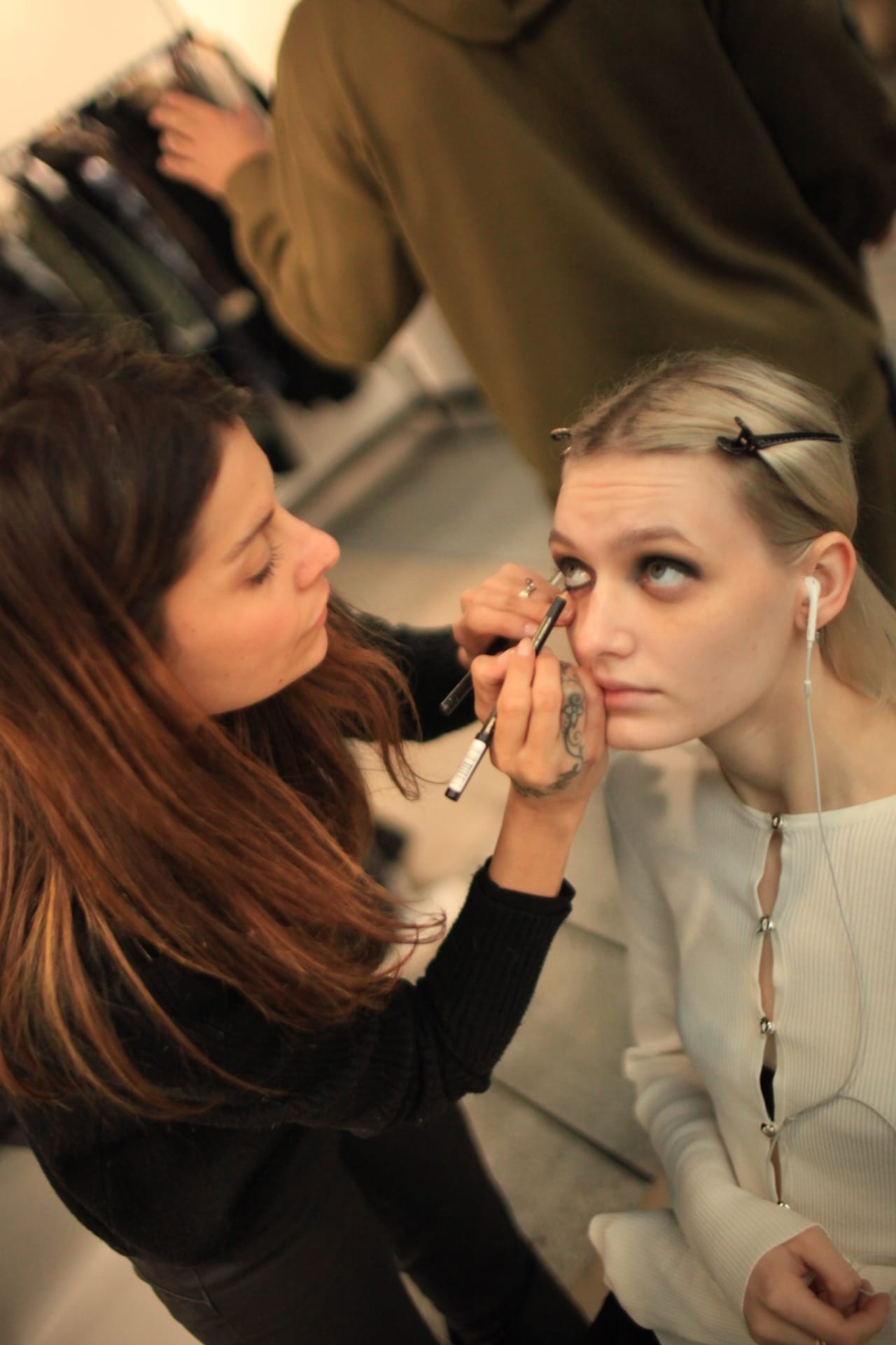 Make-up artist in formazione applica il fondotinta a una modella seduta alla postazione trucco.